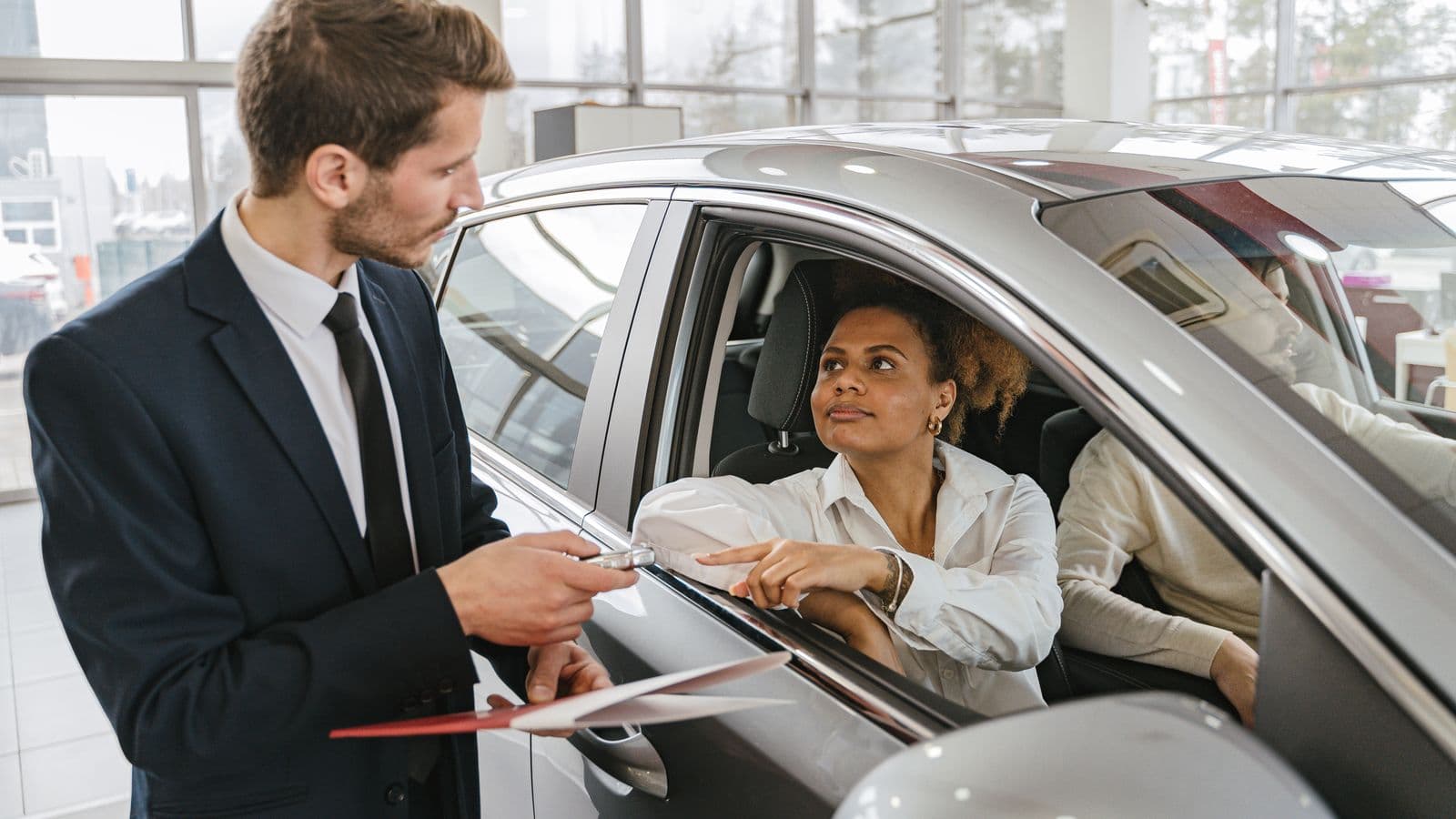 A car dealer handing keys to a woman sitting in a vehicle, representing FAVR mileage reimbursement for mobile workforces