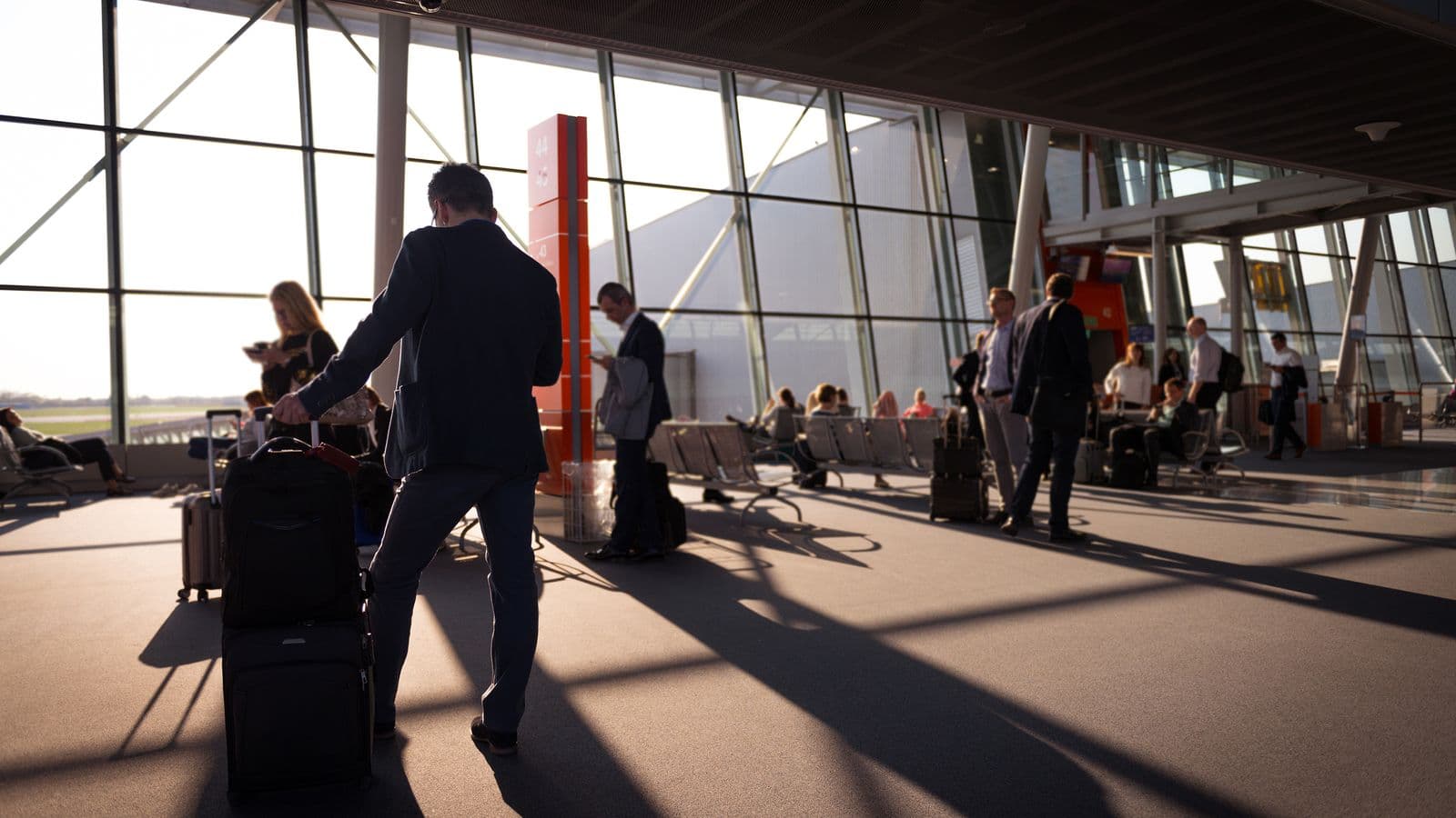 Travellers with luggage in a busy airport terminal, representing travel expense reimbursement